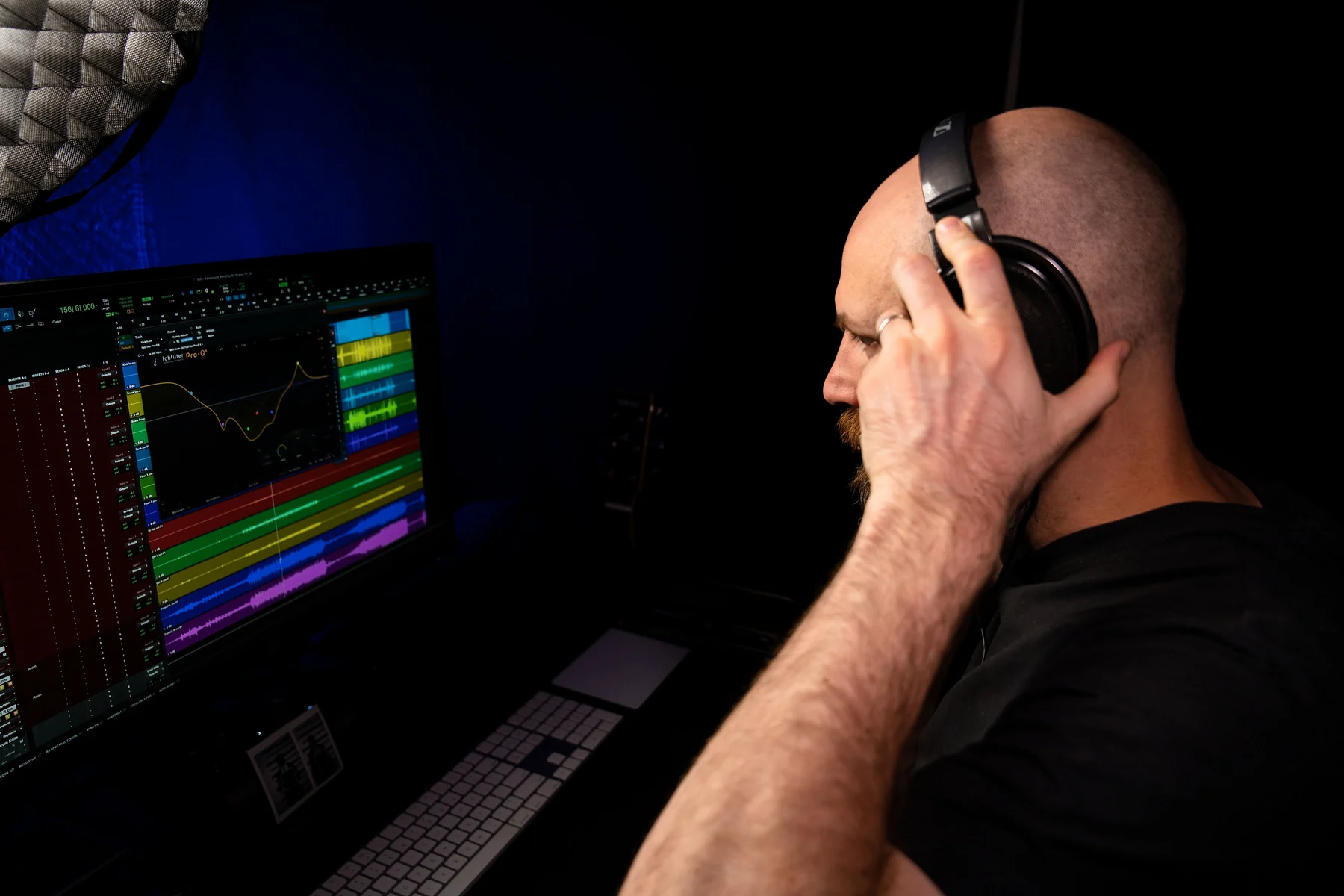 David Glenn from behind, in open-back headphones, pressing one cup to his ear